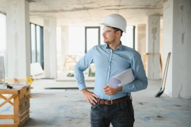 Planı ellerindeyken. Üniformalı adam inşaat alanında çalışıyor..