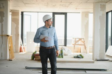 Planı ellerindeyken. Üniformalı adam inşaat alanında çalışıyor..