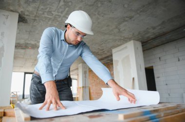 Planı ellerindeyken. Üniformalı adam inşaat alanında çalışıyor..