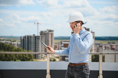 İnsan üreticisi. İnşaat alanında mimar. Tablet bilgisayarı ve kağıtları olan bir inşaatçı. Adam müfettişi inşaat kalitesini kontrol ediyor. İnşaat halindeki çok katlı binanın yanındaki mühendis..