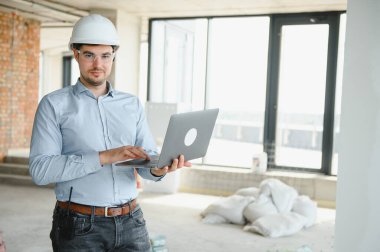 İnsan üreticisi. İnşaat alanında mimar. Tablet bilgisayarı ve kağıtları olan bir inşaatçı. Adam müfettişi inşaat kalitesini kontrol ediyor. İnşaat halindeki çok katlı binanın yanındaki mühendis..