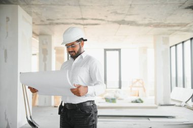 İnşaat alanında kask takan yakışıklı Hintli erkek mühendis ya da mimarın portresi..