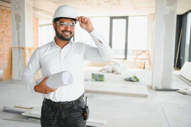 Hintli şantiye müdürü miğfer takıyor, inşaat alanında düşünüyor. Karışık ırk el işçisinin ya da mimarın portresi.