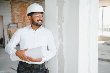 Hintli şantiye müdürü miğfer takıyor, inşaat alanında düşünüyor. Karışık ırk el işçisinin ya da mimarın portresi.