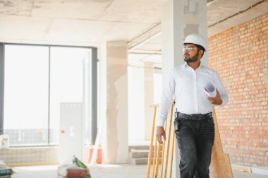 Hintli şantiye müdürü miğfer takıyor, inşaat alanında düşünüyor. Karışık ırk el işçisinin ya da mimarın portresi.