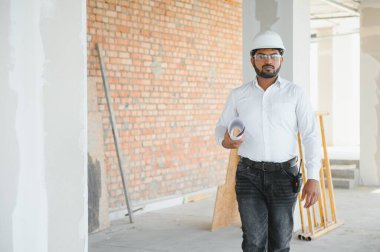 İnşaat alanında kask takan yakışıklı Hintli erkek mühendis ya da mimarın portresi..