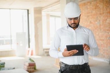 Hintli şantiye müdürü miğfer takıyor, inşaat alanında düşünüyor. Karışık ırk el işçisinin ya da mimarın portresi.