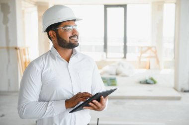 Hintli şantiye müdürü miğfer takıyor, inşaat alanında düşünüyor. Karışık ırk el işçisinin ya da mimarın portresi.