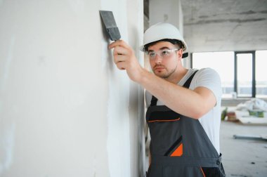 Alçı için mala kullanan alçıpan işçisi sıva beyaz duvara sıva yapıştırıyor..