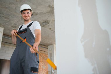 Duvarı boyayan ressamın yan görüntüsü, büyük boş alanda boya silindiri ile. Uzayı kopyala Pankart