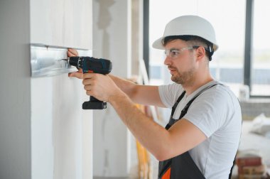 İnşaat işçisi iç bölme duvarı için metal profil yerleştirirken, arkasından bakıldığında yeni bir ev veya yenileme süreci inşa ediyor