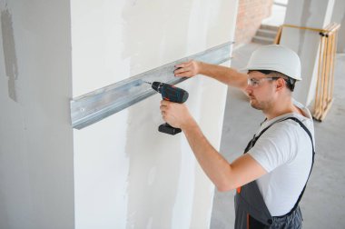 İnşaat işçisi iç bölme duvarı için metal profil yerleştirirken, arkasından bakıldığında yeni bir ev veya yenileme süreci inşa ediyor