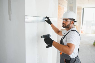 İnşaat işçisi iç bölme duvarı için metal profil yerleştirirken, arkasından bakıldığında yeni bir ev veya yenileme süreci inşa ediyor