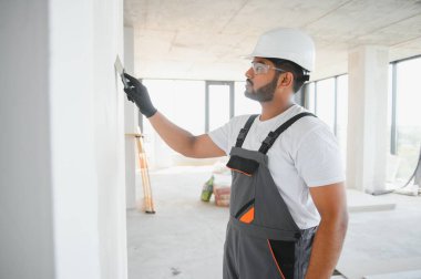 İş tulumlu erkek müteahhit inşaat malası kullanarak duvarı sıvamış..