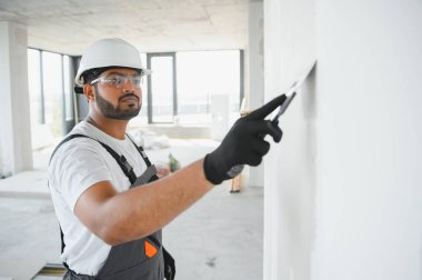 İş tulumlu erkek müteahhit inşaat malası kullanarak duvarı sıvamış..