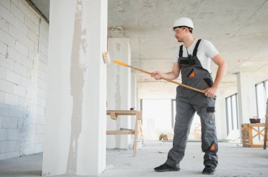 Duvarı boyayan ressamın yan görüntüsü, büyük boş alanda boya silindiri ile. Uzayı kopyala Pankart