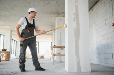 Duvarı boyayan ressamın yan görüntüsü, büyük boş alanda boya silindiri ile. Uzayı kopyala Pankart