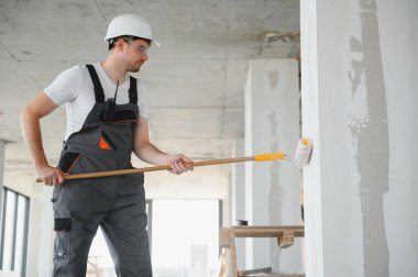 Duvarı boyayan ressamın yan görüntüsü, büyük boş alanda boya silindiri ile. Uzayı kopyala Pankart