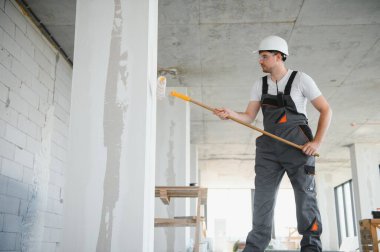 Duvarı boyayan ressamın yan görüntüsü, büyük boş alanda boya silindiri ile. Uzayı kopyala Pankart
