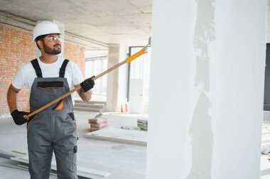 Hintli bir apartman tamircisi silindirle beyaz bir duvar boyuyor..