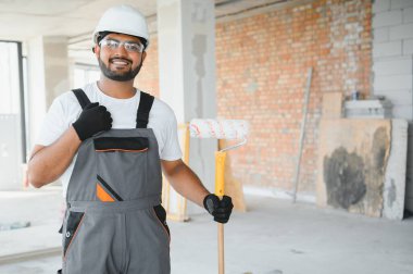 Hintli bir apartman tamircisi silindirle beyaz bir duvar boyuyor..