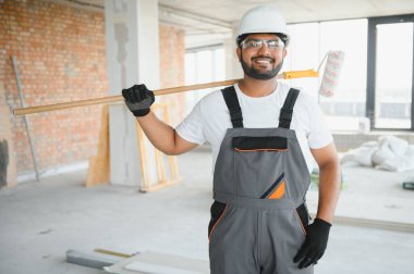 Hintli bir apartman tamircisi silindirle beyaz bir duvar boyuyor..