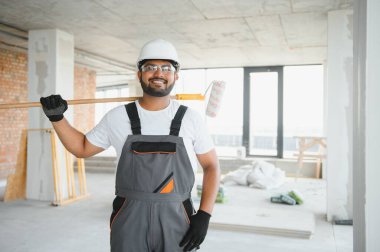 Hintli bir apartman tamircisi silindirle beyaz bir duvar boyuyor..