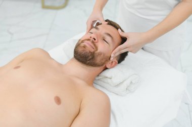 Stres önleyici baş masajı. Yakışıklı adam masaj salonunda kafa masajı yaparken rahatlıyor..