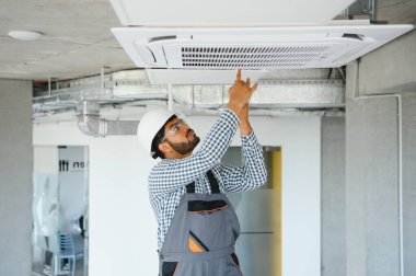 Hintli erkek işçi tavana monte edilmiş klimayı inceliyor..