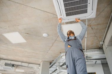 Hintli erkek işçi tavana monte edilmiş klimayı inceliyor..