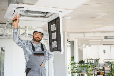 Hintli erkek işçi tavana monte edilmiş klimayı inceliyor..