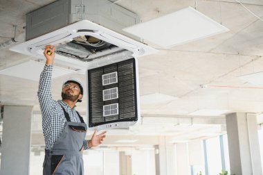 Hintli erkek işçi tavana monte edilmiş klimayı inceliyor..