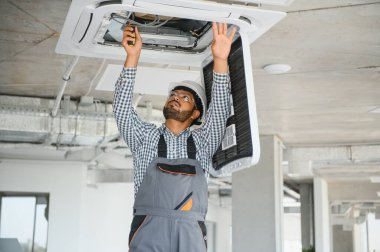Hintli erkek işçi tavana monte edilmiş klimayı inceliyor..