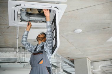 Hintli erkek işçi tavana monte edilmiş klimayı inceliyor..