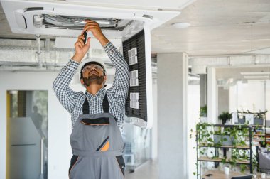 Hintli erkek işçi tavana monte edilmiş klimayı inceliyor..