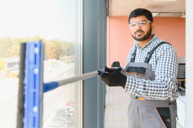 Erkek profesyonel temizlik işçisi, özel ekipmanlı bir mağazanın camlarını ve pencerelerini temizler..