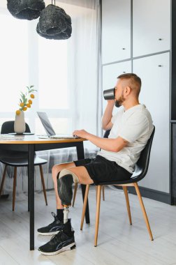 Diz üstü bacak protezi üzerinde protez bacak sakatlığı olan bir adam evde dizüstü bilgisayar kullanarak yapay bir cihaz kullanıyor. Ampütasyon engelli insanlar günlük hayatta.