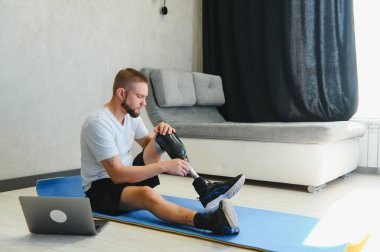 Sportif formda, bacağı sakat, protez protezli bir genç adam evde dizüstü bilgisayar kullanarak antrenman yapıyor. Engelliler için özel online spor dersleri.