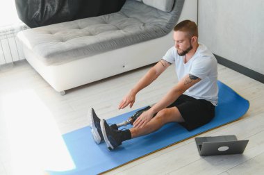 Sportif formda, bacağı sakat, protez protezli bir genç adam evde dizüstü bilgisayar kullanarak antrenman yapıyor. Engelliler için özel online spor dersleri.