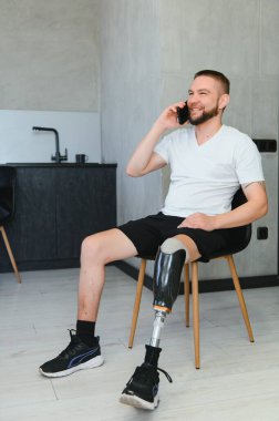 Protez bacaklı genç bir adam evde oturmuş telefonla konuşuyor..