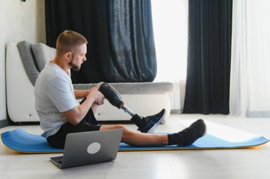 Protez bacaklı bir adam evdeki paspasın üstünde spor egzersizleri yapıyor. Rehabilitasyon kavramı.