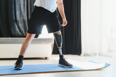 Sportif formda, protez bacak sakatlığı protezli, bacağı kesilmiş genç bir adam evde hasırla tahta egzersizi yapıyor. Engelliler için özel spor eğitimi. Yakın çekim.