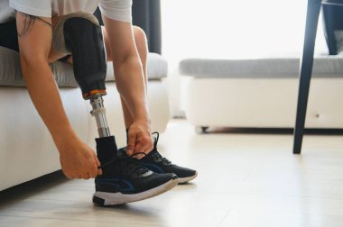 Dizinde protez bacak sakatlığı olan bir erkek bacak protezi takıyor. Kanepede oturuyor. Kapatın. Ampütasyon engelli insanlar günlük yaşam konsepti.