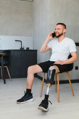 Protez bacaklı genç bir adam evde oturmuş telefonla konuşuyor..