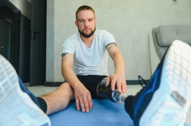 Protez bacaklı bir adam evdeki paspasın üstünde spor egzersizleri yapıyor. Rehabilitasyon kavramı.