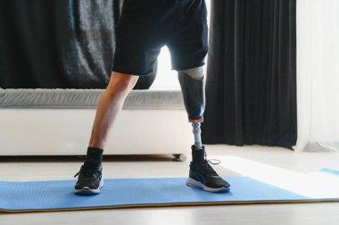Protez bacaklı bir adam evdeki paspasın üstünde spor egzersizleri yapıyor. Rehabilitasyon kavramı.