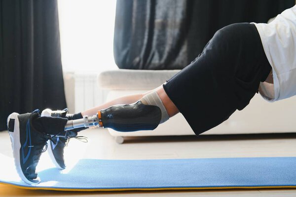 Мужчина с протезной ногой делает дома спортивные упражнения на коврике. Концепция реабилитации.