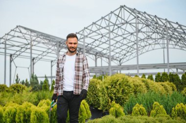 Bahçe alışveriş merkezinin erkek çalışanı ürünü denetliyor. Çiçek saksısı olan departman müşterilerine tavsiye vermeye hazırlanıyor..