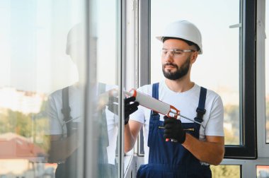 Worker sealing plastic window with caulk indoors. Installation process.