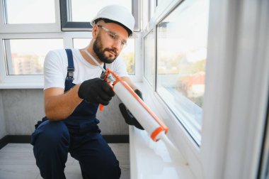 Worker sealing plastic window with caulk indoors. Installation process.